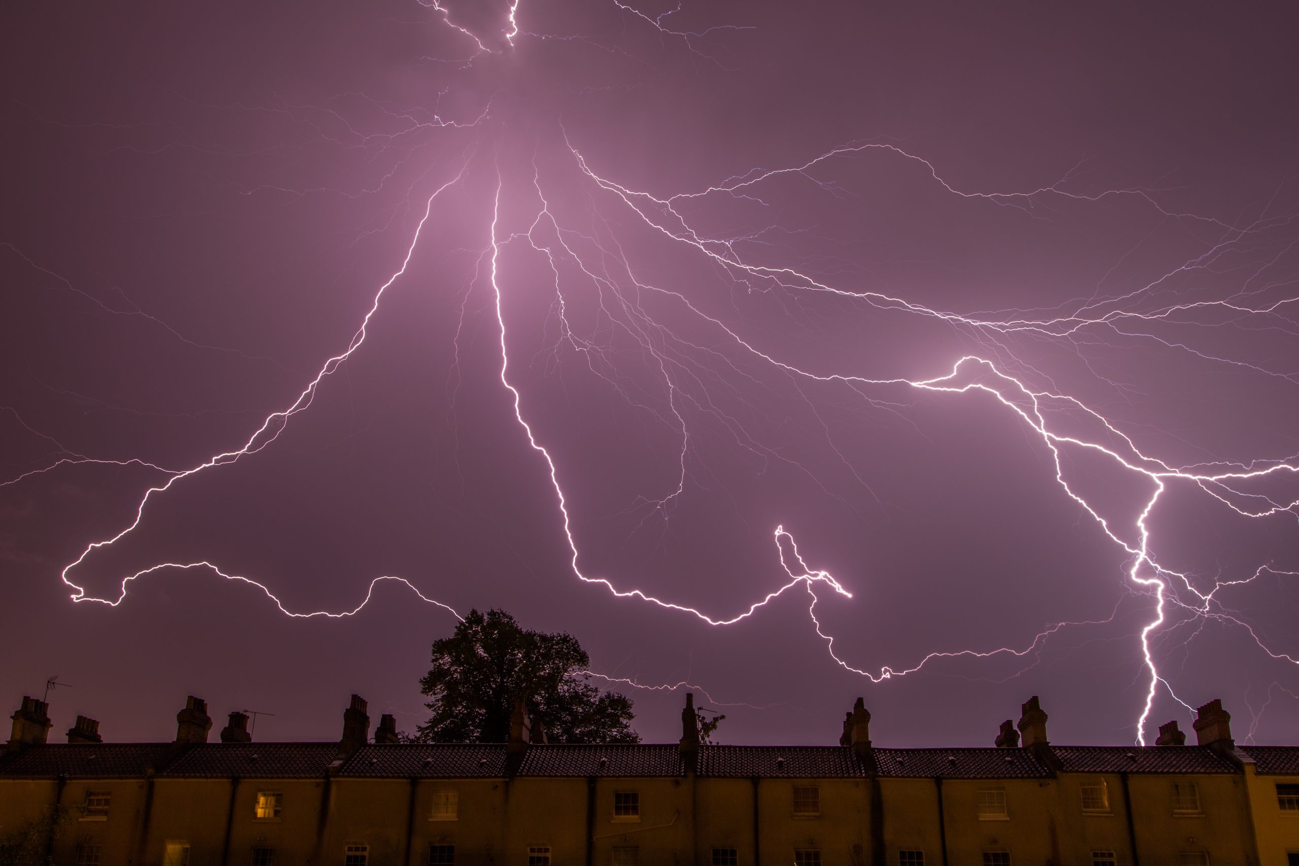 Lightning striking in a stormy sky above residential rooftops, illustrating potential HVAC challenges during severe weather.