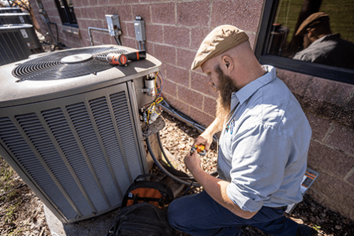 Technician repairing air conditioning unit with tools, showcasing HVAC expertise by Acosta Heating, Cooling & Electrical.