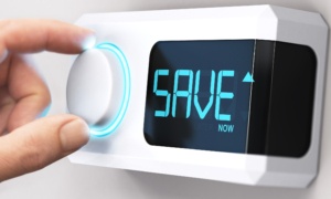 Hand turning a thermostat knob with screen reading "Save Now"