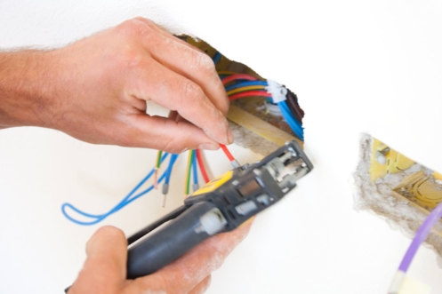 Technician's hands using wire strippers on colored electrical wires for home surge protection installation.